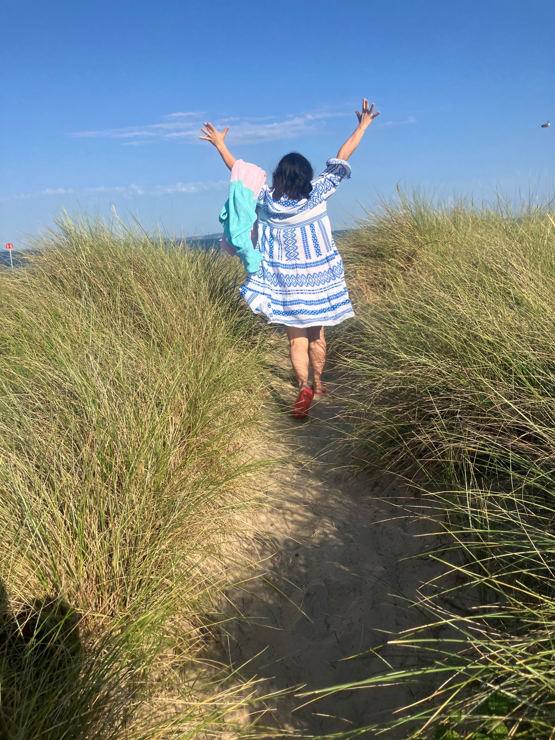 lady in dress walking through grass from back with arms in air