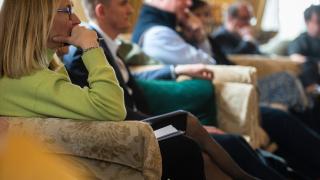 Group of people sitting on sofas listening to speaker.