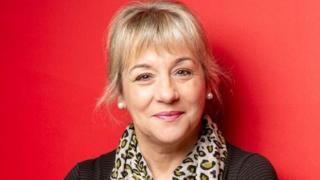 Dame Martina, smiling in front of red backdrop