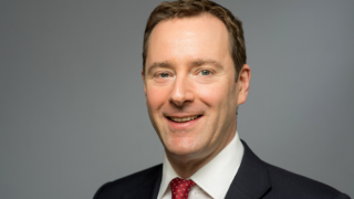 Man in suit with red tie smiling.