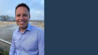 Nathan Powell standing in a blue shirt and smiling